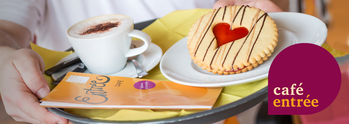 Tablett mit einer Tasse Kaffee, Gebäck mit rotem Herz und Flyer Café Entrée. 